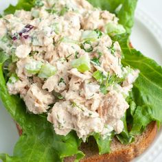 a white plate topped with lettuce and chicken salad next to crackers on a table