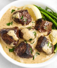 a white bowl filled with meat and gravy next to asparagus