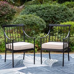 two black chairs sitting on top of a blue and white rug in front of bushes