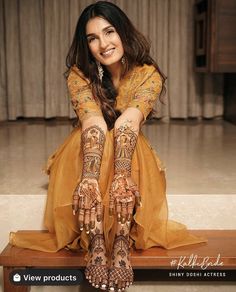 a woman sitting on top of a wooden bench wearing henna and holding her hands up