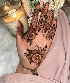 a woman's hand with henna on it next to a candle and flowers