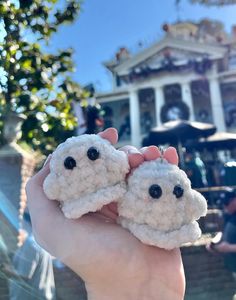 two crocheted sheep are held up in front of a building with black eyes