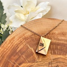 a gold origami necklace sitting on top of a piece of wood next to a white flower