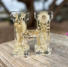 two glass vases sitting on top of a wooden table next to each other with flowers in them