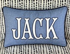 a blue and white pillow with the word jack on it sitting on a patterned couch