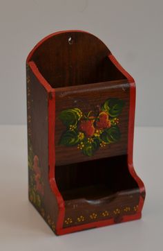 a small wooden box with flowers painted on the front and sides, sitting on a white surface