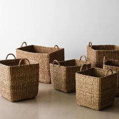 four woven baskets sitting next to each other on the floor in front of a white wall