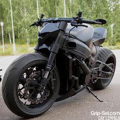 a black motorcycle parked on top of a parking lot next to some grass and trees