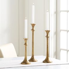 three candles sitting on top of a white table next to a window in a room