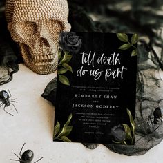 a black and white wedding card with roses on it next to a fake human skull