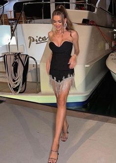 a woman in a short black dress walking on the floor next to a boat at night