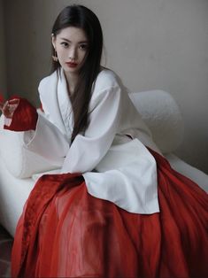 a woman sitting on top of a bed wearing a red and white dress with long sleeves