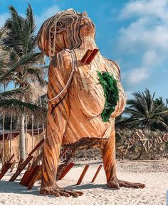 a large wooden bear statue sitting on top of a sandy beach next to palm trees