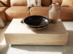 a wooden table with a black bowl on it and a brown couch in the background