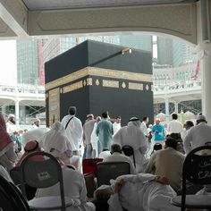 many people are sitting in chairs around the ka'bah, which is surrounded by tall buildings