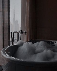 a bathtub filled with foam in front of a window overlooking a cityscape