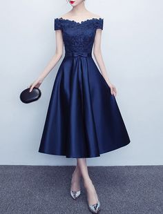 a woman wearing a blue dress with off the shoulder sleeves and lace detailing, standing in front of a white wall