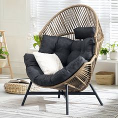 a wicker chair with black cushions and white pillows on it in a living room