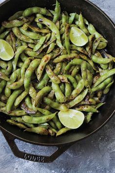 sesame blistered edamame in a skillet with lime wedges on the side