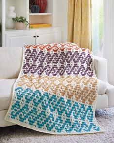 a white couch sitting next to a window covered in a multicolored crocheted blanket