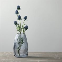 a glass vase filled with blue flowers on top of a wooden table next to a white wall