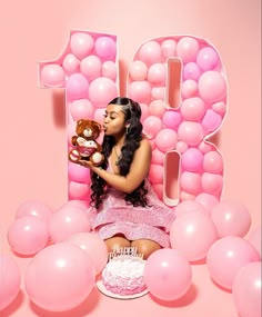 a woman holding a teddy bear sitting in front of a pink balloon wall with the number 10 on it