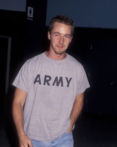 a man standing with his hands in his pockets and wearing an army t - shirt