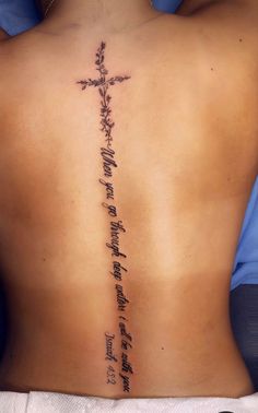 the back of a woman with a cross tattoo on her lower back, and words written in cursive writing