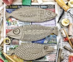 two fish shaped wooden carvings sitting on top of a newspaper next to scissors and other crafting supplies