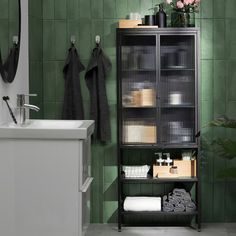 a bathroom with green tile walls and white fixtures on the shelves, along with black towel racks