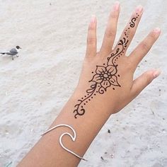 a woman's hand with a henna tattoo on it and a seagull in the background