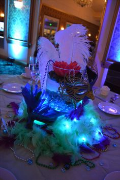 a table topped with lots of feathers on top of a white table cloth covered in blue and green lights