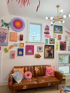 a brown leather couch sitting under a window next to a wall covered in pictures and paintings