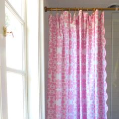 a pink and white shower curtain hanging from a metal rod in front of a window