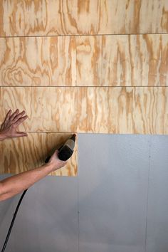 a man is using a brush to paint the wood paneled wall in his home