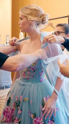 a woman in a blue dress is getting her hair done by a man with glasses