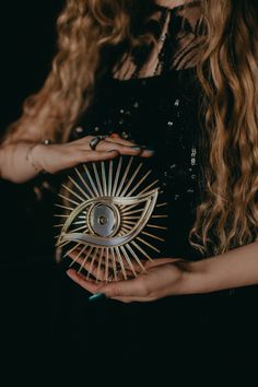 a woman with long hair holding an object in one hand and wearing rings on the other