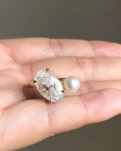 a woman's hand holding an engagement ring with a pearl on the side and a diamond in the middle