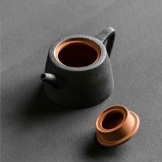 a teapot and cup sitting on a gray surface next to each other, with the lid off