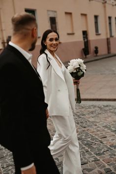 a bride and groom are walking down the street in their wedding attire, smiling at each other