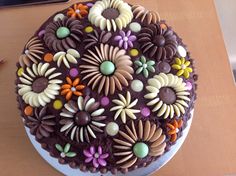 a chocolate cake decorated with colorful flowers on top of a wooden table next to a laptop computer