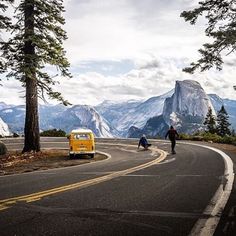 a yellow van is parked on the side of a road with mountains in the background