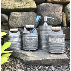 four metal canisters with toothbrushes in them sitting on some rocks and gravel