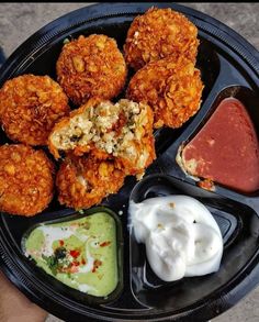 a black plate topped with different types of food and dipping sauces on top of it