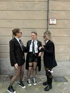 three young women dressed in short shorts and high heels talking to each other on the sidewalk