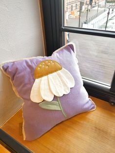 a purple pillow with a white flower on it sitting next to a window sill