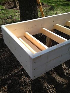 an unfinished bed frame sitting in the dirt next to a tree and grass area with trees