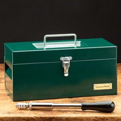 a green tool box with a handle and two wrenches in front of it on a wooden table