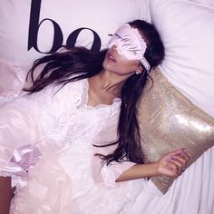 a woman laying on top of a bed wearing a white mask and holding a pillow