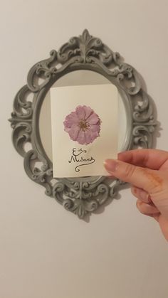 a person holding up a card with a flower on it in front of a mirror